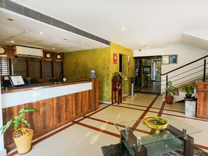 A hotel reception area with a wooden reception desk, a clock, and a staircase leading to another floor. - Treebo Time Square Marine Drive (Kanayannur)