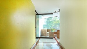 A hallway with a yellow wall, a glass door leading to a balcony with wicker furniture. - Treebo Time Square Marine Drive (Kanayannur)