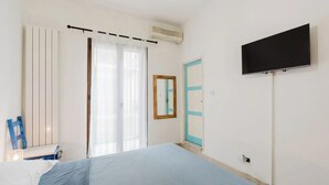 Een slaapkamer met een bed, een televisie, een raam met gordijnen, een radiator en een deur.