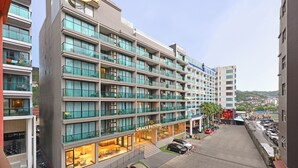 A multi-story hotel with a prominent sign reading "GRACE PATONG". It features balconies with glass railings, a ground-level restaurant, and a parking area with cars. - Grace Patong Hotel (Patong)