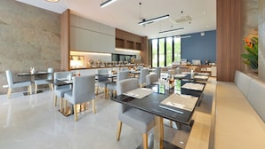A modern dining area with multiple tables and chairs, a kitchen in the background, and large windows allowing natural light. - Grace Patong Hotel (Patong)