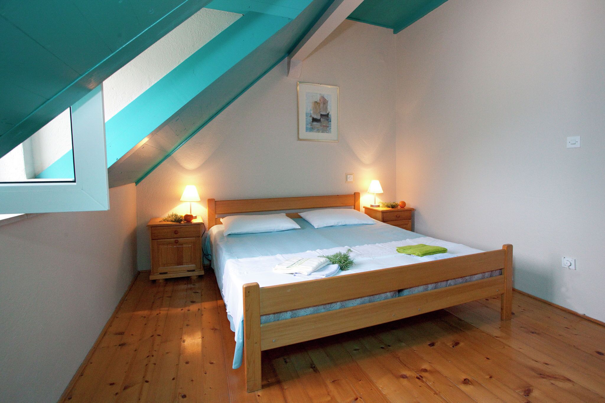 Un dormitorio con una cama de madera, dos lámparas de noche, un cuadro enmarcado en la pared y un tragaluz.