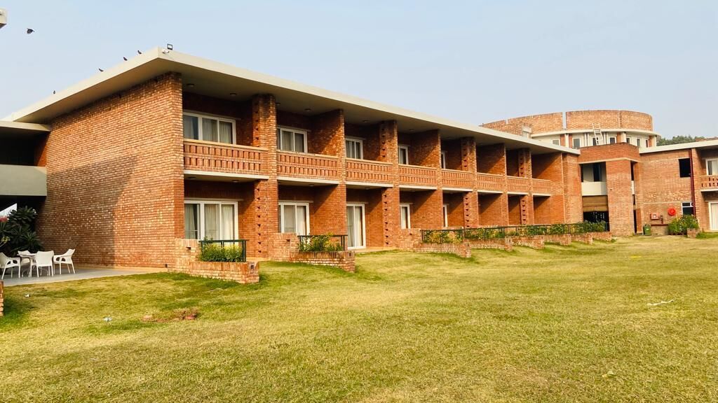 A multi-story brick building with a flat roof and a circular structure to the right.