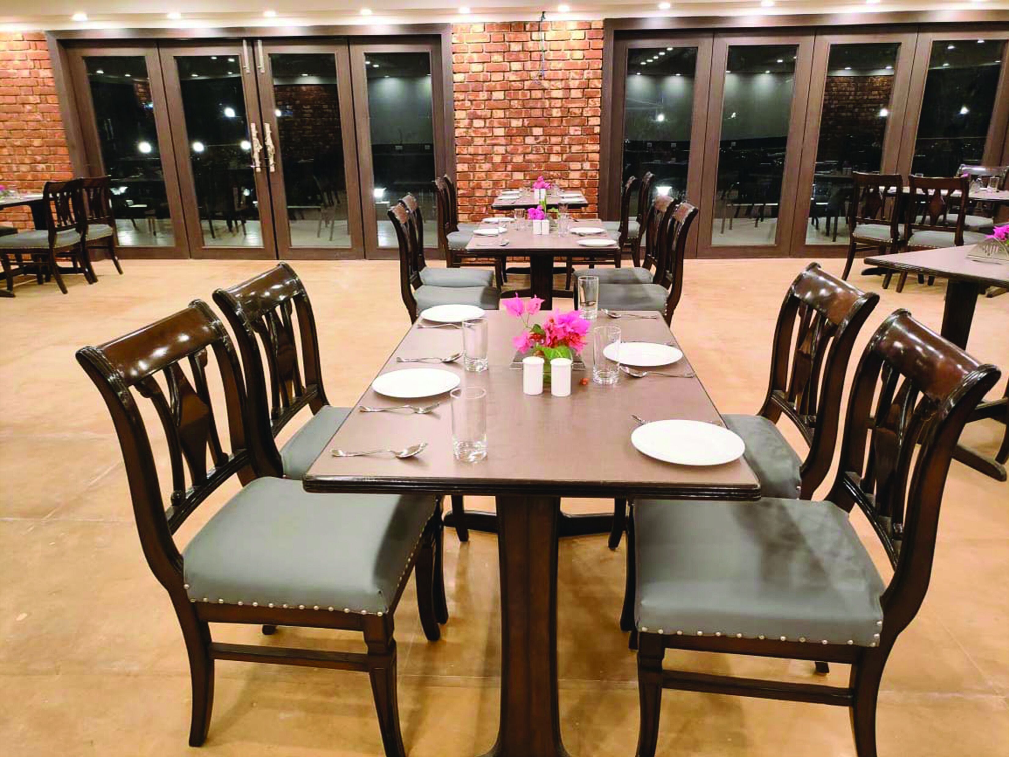 An indoor dining area with brick walls, large windows, and multiple tables set for dining.