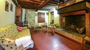 A cozy living room with a fireplace, wooden beams, a sofa, and a stone wall. - Holiday Home Monte Santa Maria Pool Retreat (Monte sta Maria Tiberina)