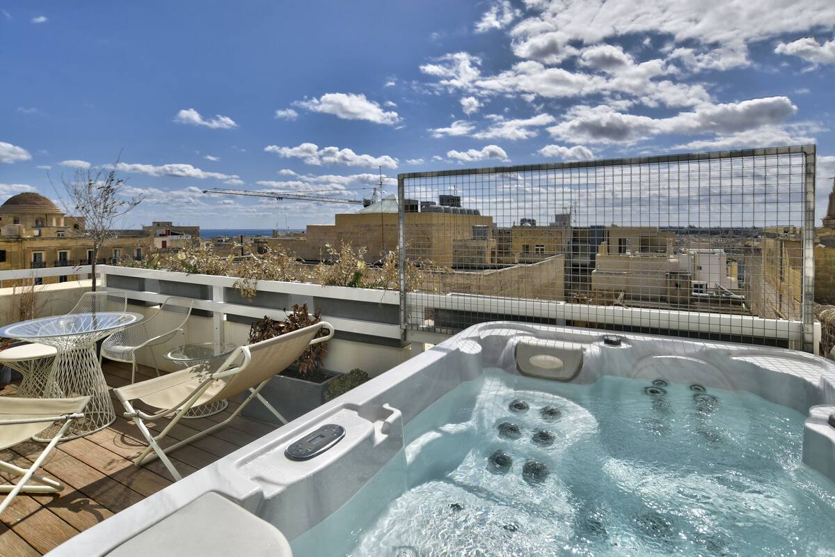 Terraza en la azotea con jacuzzi, sillones de descanso y una mesa.
