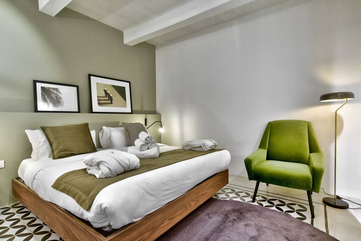 Un dormitorio moderno con una cama de madera, un sillón verde y dos cuadros en la pared.