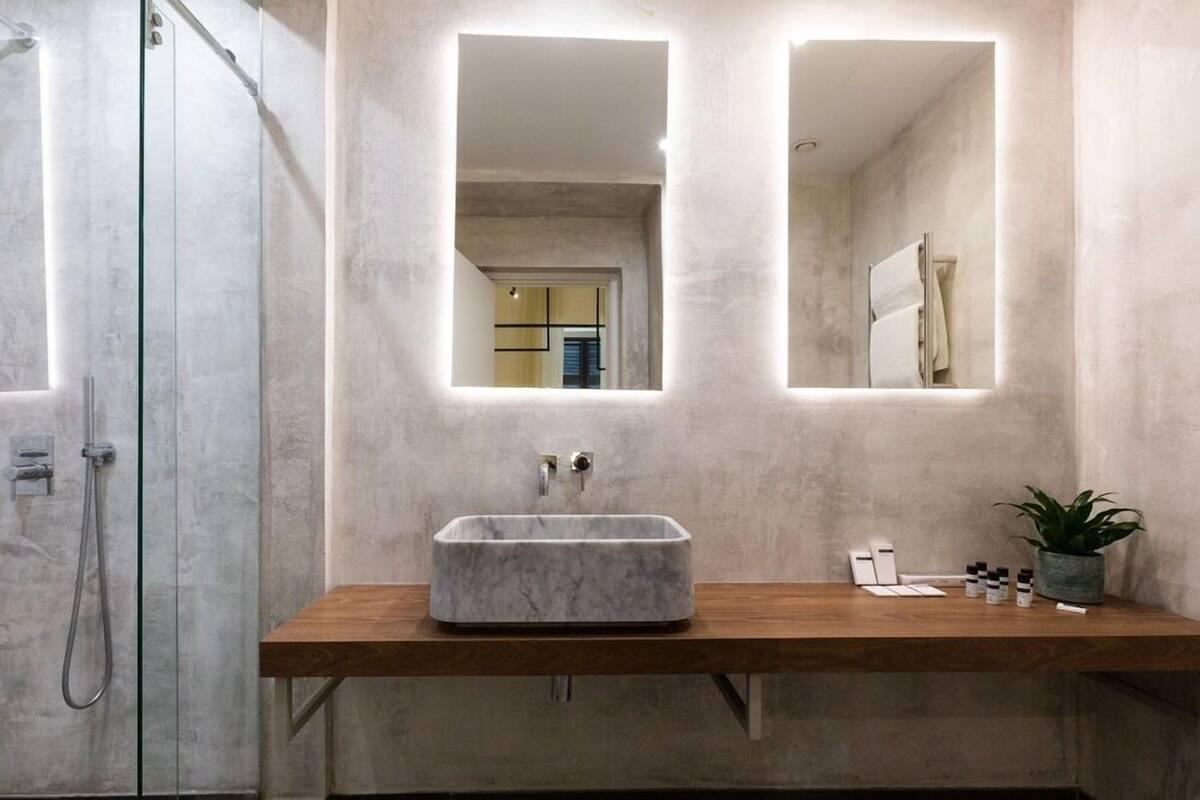 Un baño moderno con lavamanos de mármol, encimera de madera y dos espejos fijos en la pared.