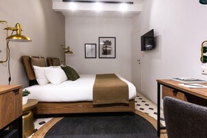 Quarto moderno com cama, mesa de cabeceira, luminária, televisão e obra de arte na parede.