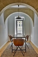 Uma área de refeições com mesa e cadeiras, teto abobadado e vista através de uma porta aberta.