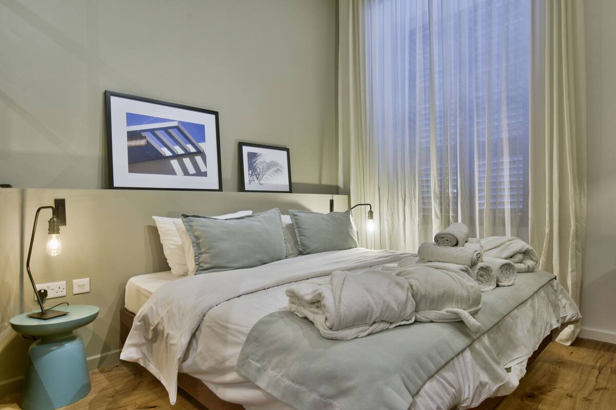 Una cama bien hecha con almohadas y una colcha, una mesita de noche con lámpara, y dos cuadros en la pared.