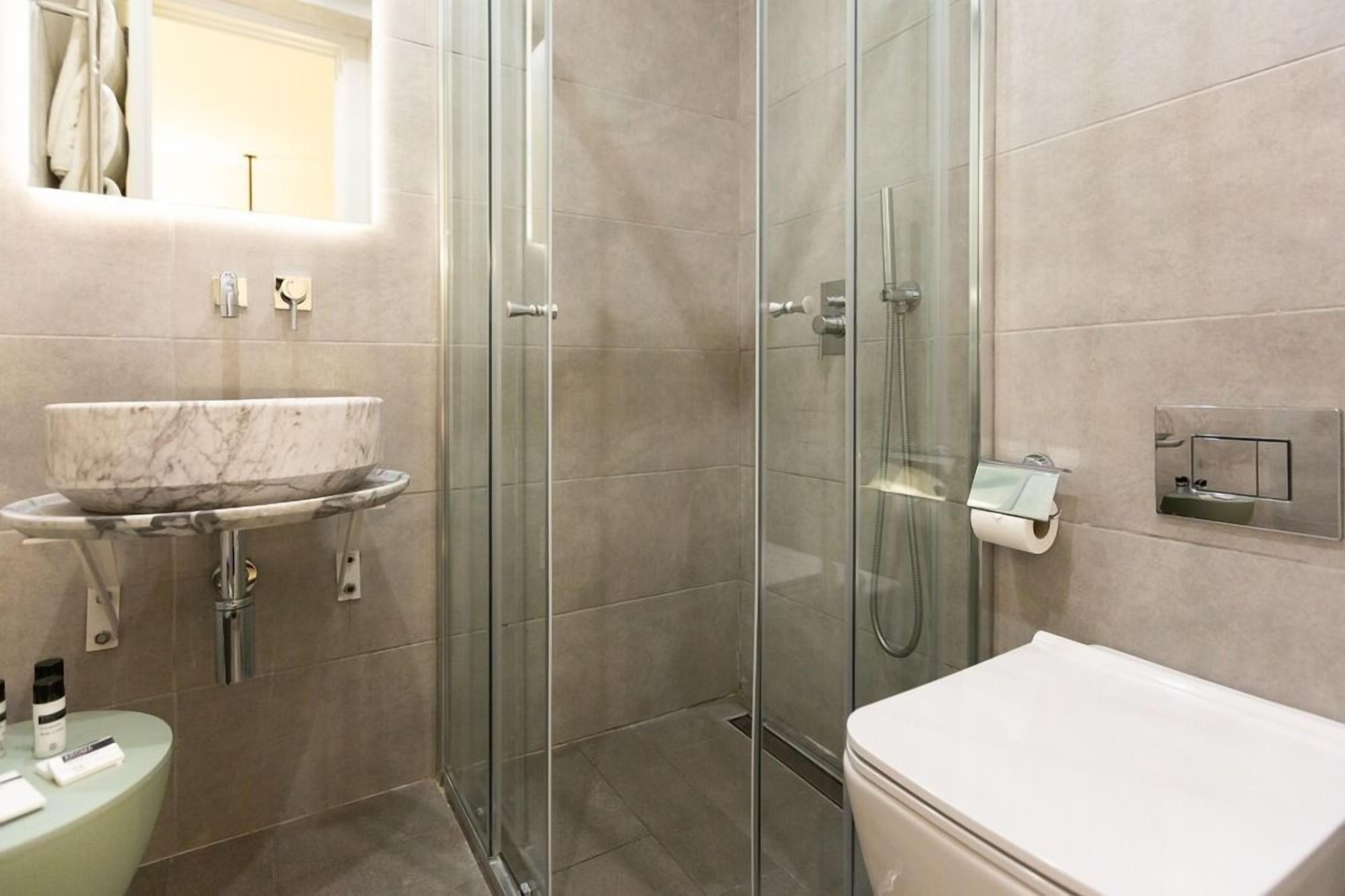 A modern bathroom with a glass-enclosed shower, a marble sink, and a toilet.