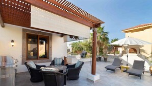 Une terrasse extérieure dotée d’un barbecue, de meubles en osier et d’une pergola.