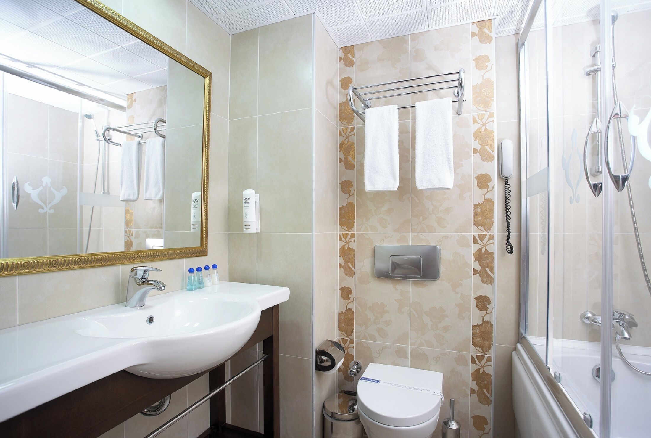 A bathroom with a white sink, mirror, and toilet, a glass shower enclosure, and a towel rack with two towels.