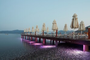 A pier with umbrellas and tables extending into calm water, with mountains in the background. - Emre Hotel And Emre Beach Hotel (Marmaris)