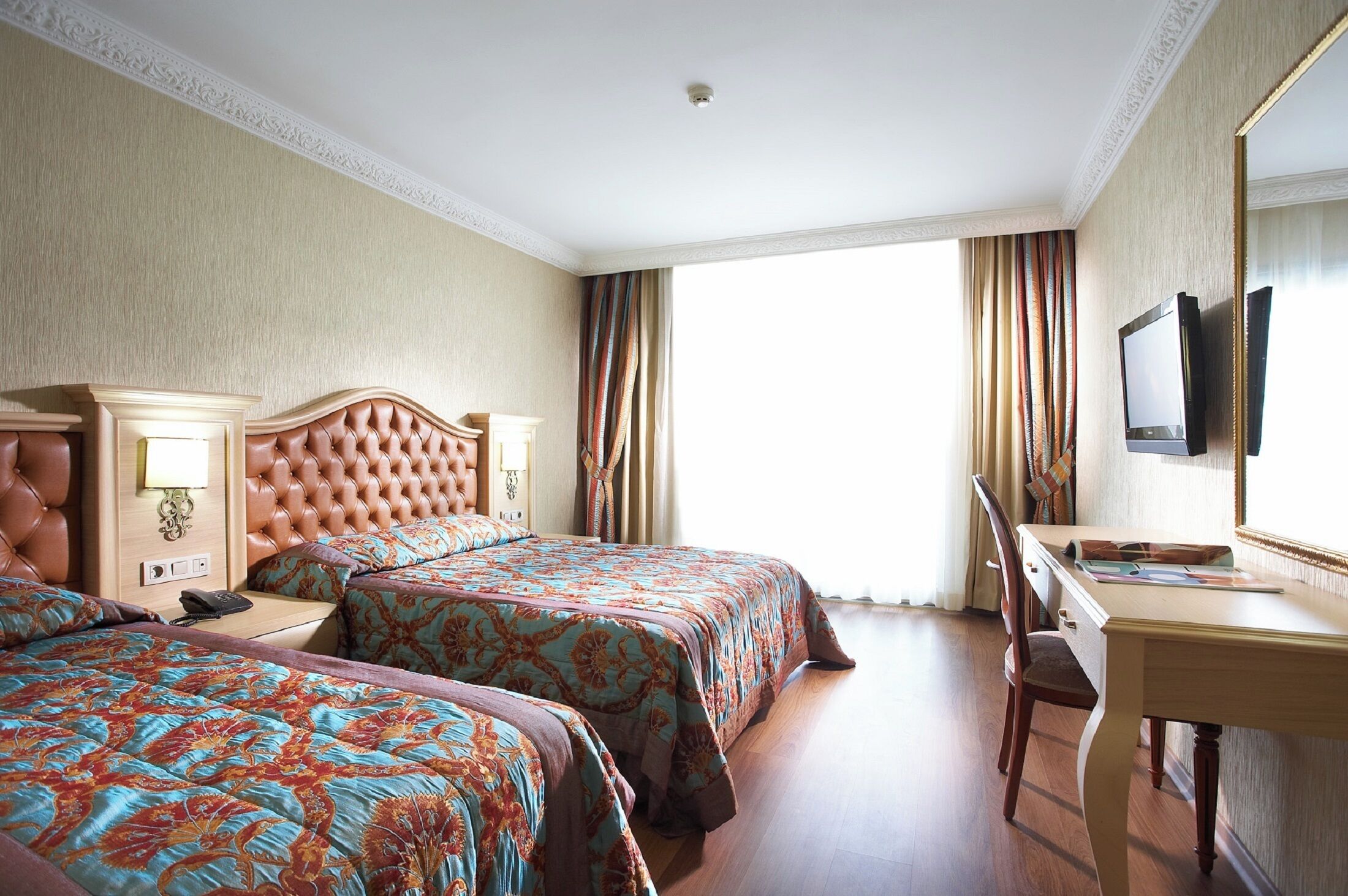 A hotel room with two beds, a desk, a chair, a television, and a window with curtains.