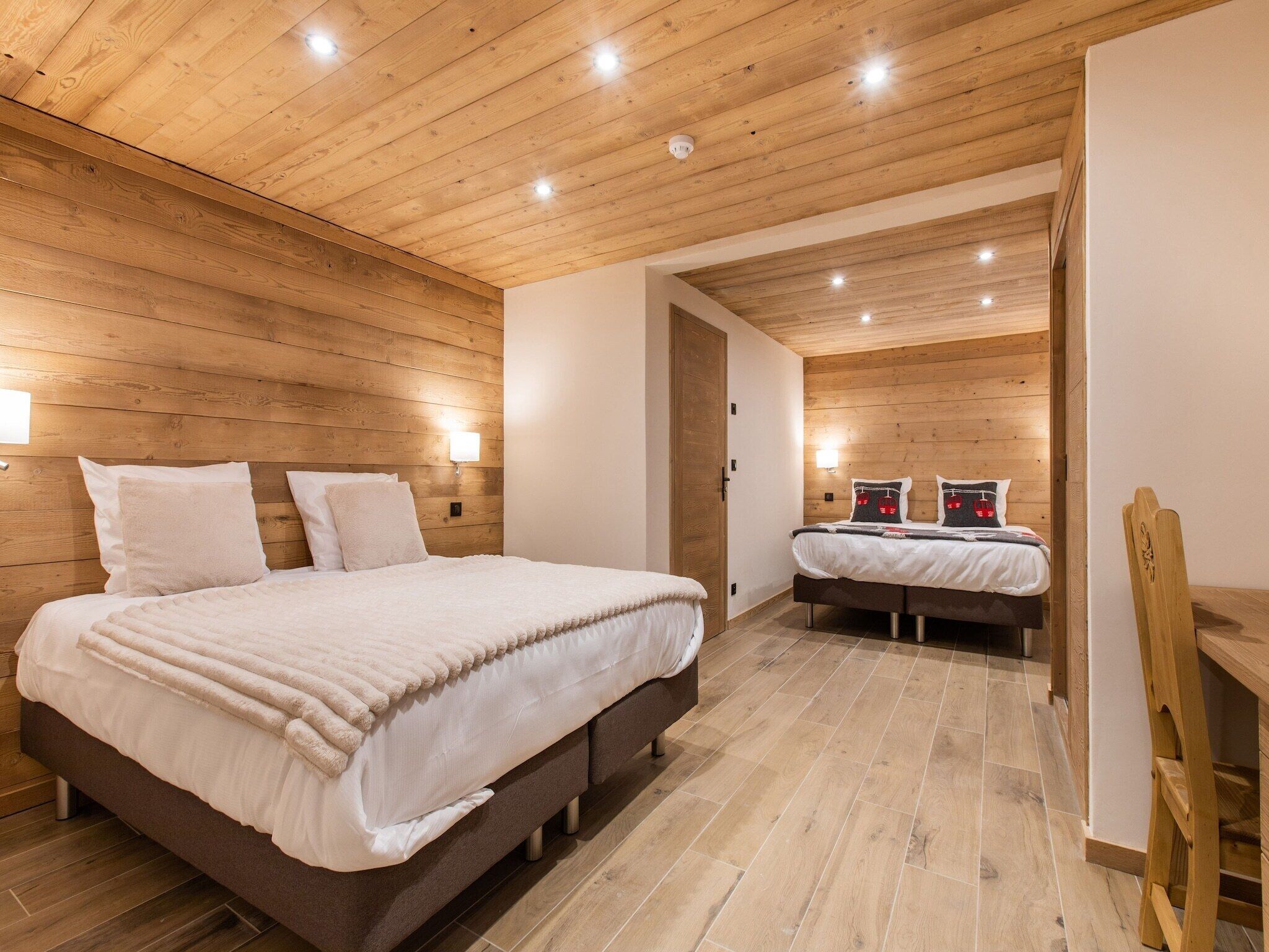 Une chambre moderne avec des murs recouverts de panneaux de bois, un grand lit avec une literie blanche, un plus petit lit et une chaise en bois.
