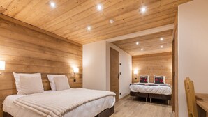A modern bedroom with wooden panel walls, a large bed with white bedding, a smaller bed, and a wooden chair.