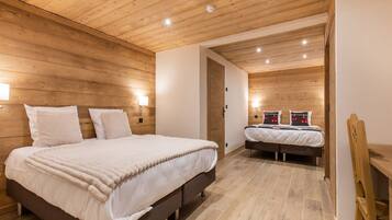 Une chambre moderne avec des murs recouverts de panneaux de bois, un grand lit avec une literie blanche, un plus petit lit et une chaise en bois.