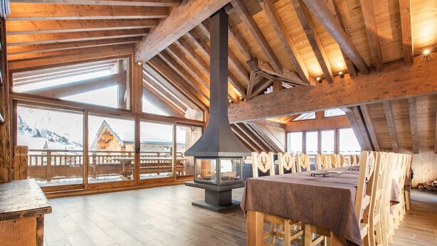 A spacious wooden interior with a large fireplace, wooden tables, and benches.