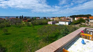 A balcony with a table and chairs, overlooking a green landscape and a coastal town.