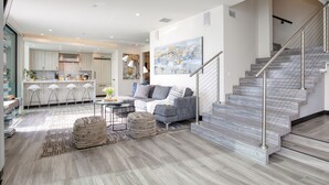 A modern living room with a grey sofa, a coffee table, and a rug. There is a staircase with a metal railing leading to an upper floor.