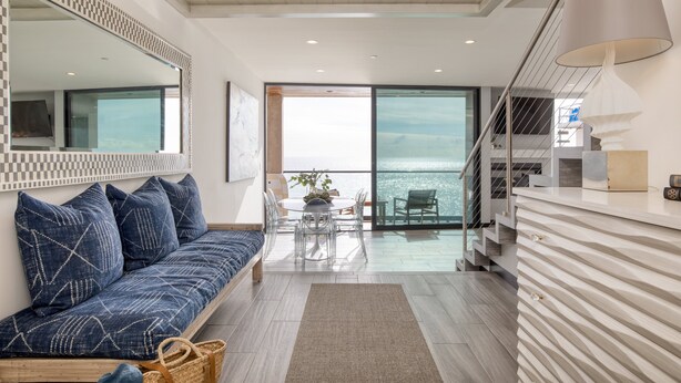 A modern living room with a sofa, dining table, and a view of the sea.