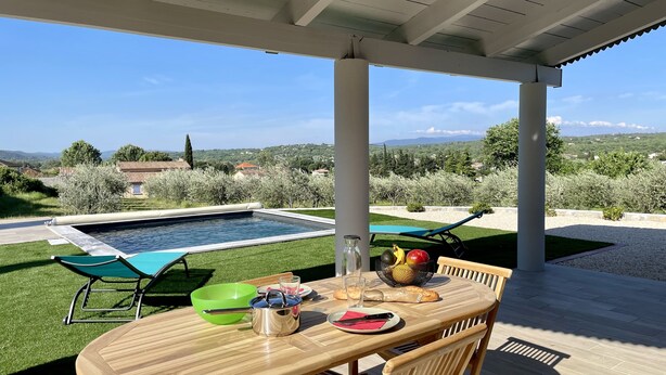 An outdoor patio with a pool, a table set for dining, and a view of the countryside. - Gîte de la Picholine 3* (Ruoms)