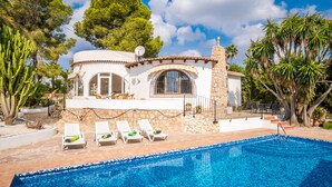 A white villa with a pool, surrounded by trees and a clear sky.