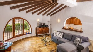 A living room with a wooden ceiling, a grey sofa, a wooden cabinet, and a television.