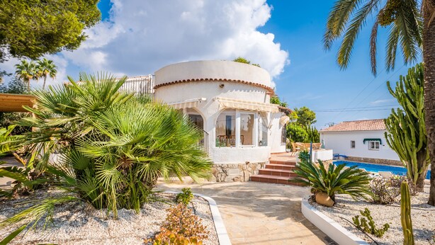 A white building with a curved roof, surrounded by palm trees and a swimming pool.
