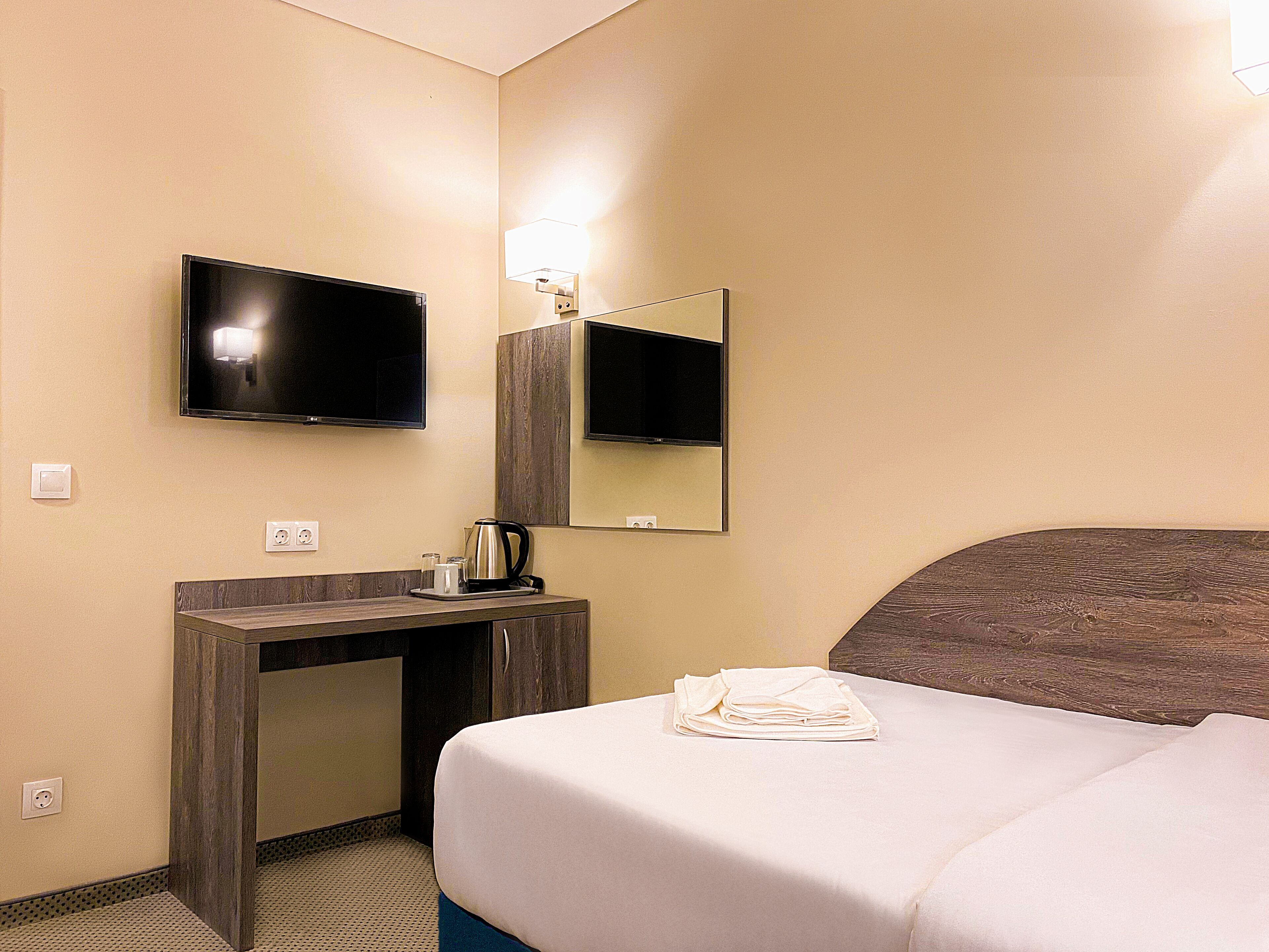 Habitación de hotel con cama, escritorio con hervidor, televisor de pantalla plana y espejo.