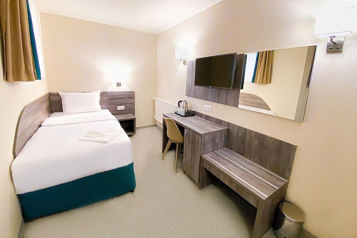 Quarto de hotel com cama, escrivaninha, cadeira e televisão na parede.