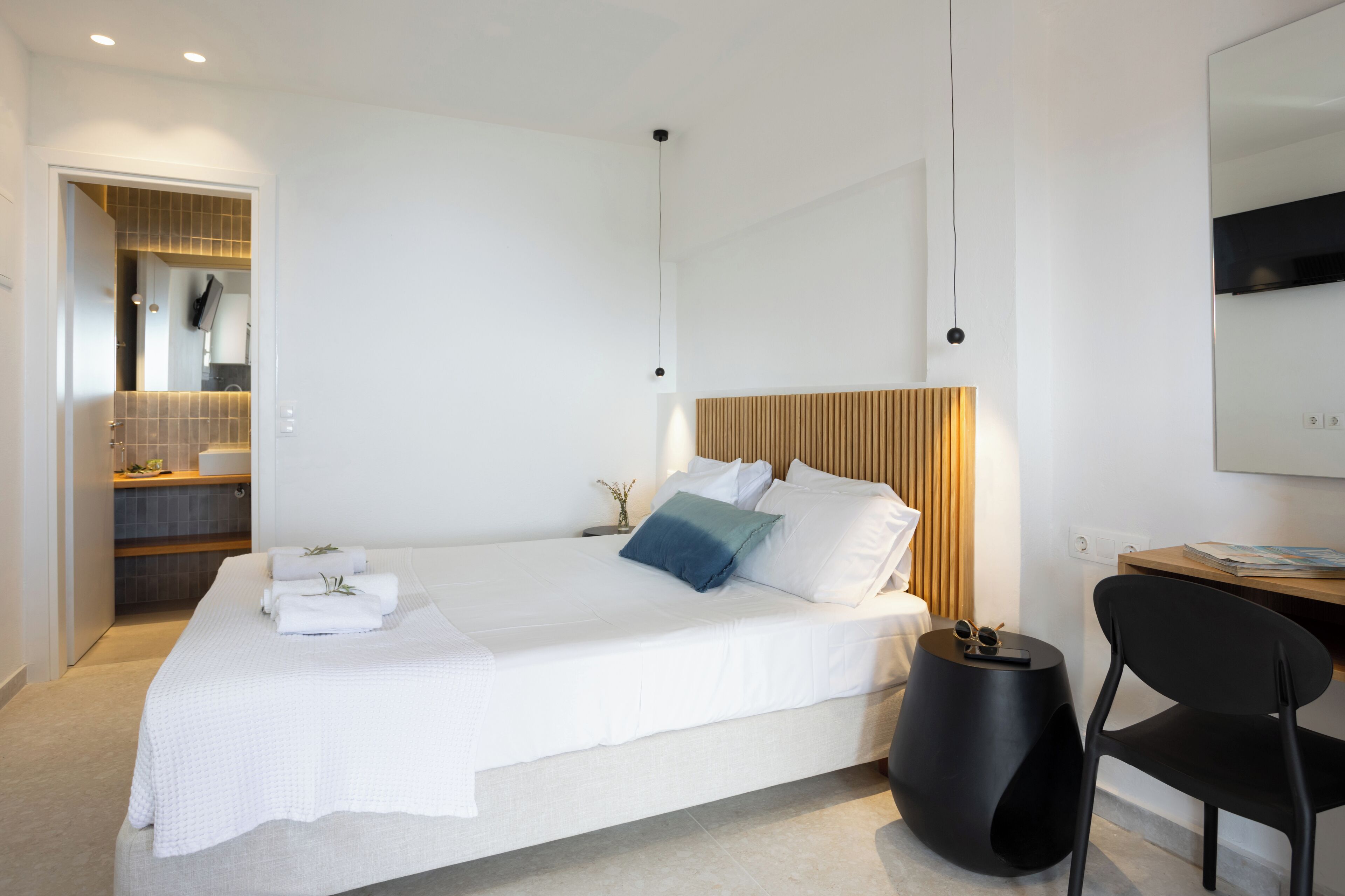A modern hotel room with a large bed, a wooden headboard, a small side table, and a black chair.