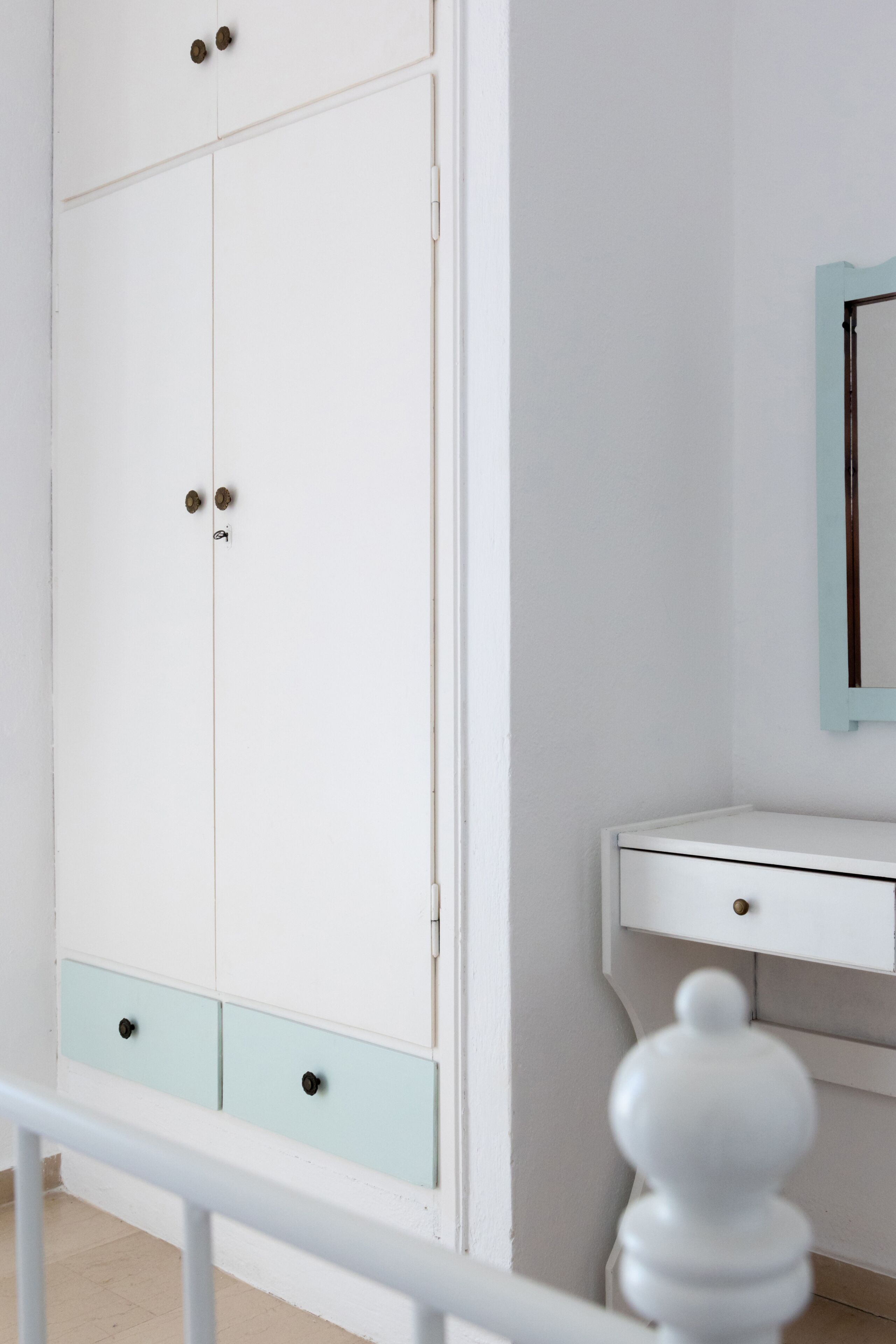 A white wardrobe with two doors and a light blue drawer, a white bedside table, and a mirror with a light blue frame.