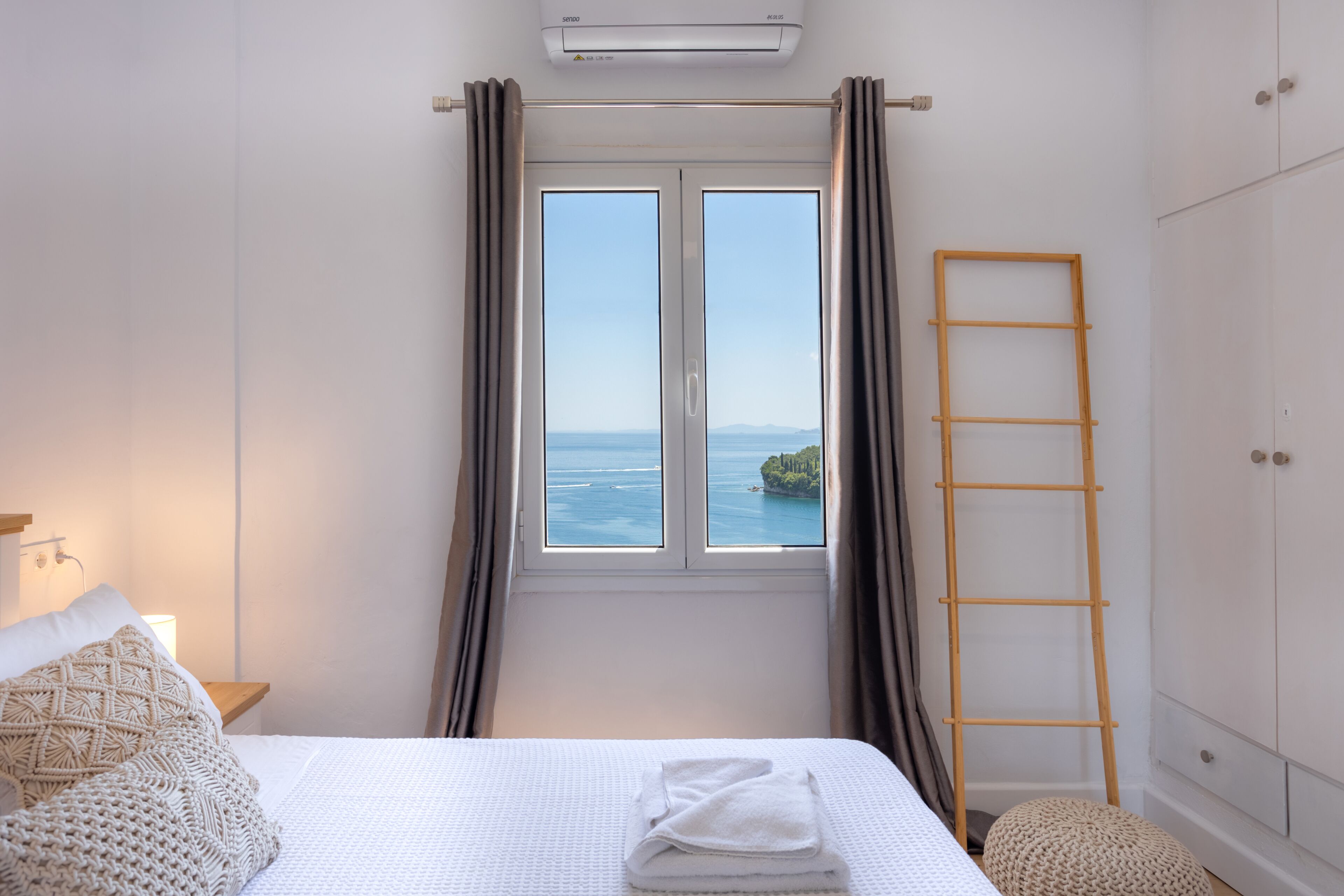A bedroom with a bed, a window with curtains, a wooden ladder, and a wardrobe.