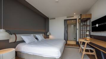 A modern hotel room with a large bed, bedside tables, a desk with a chair, a television, and a wardrobe.