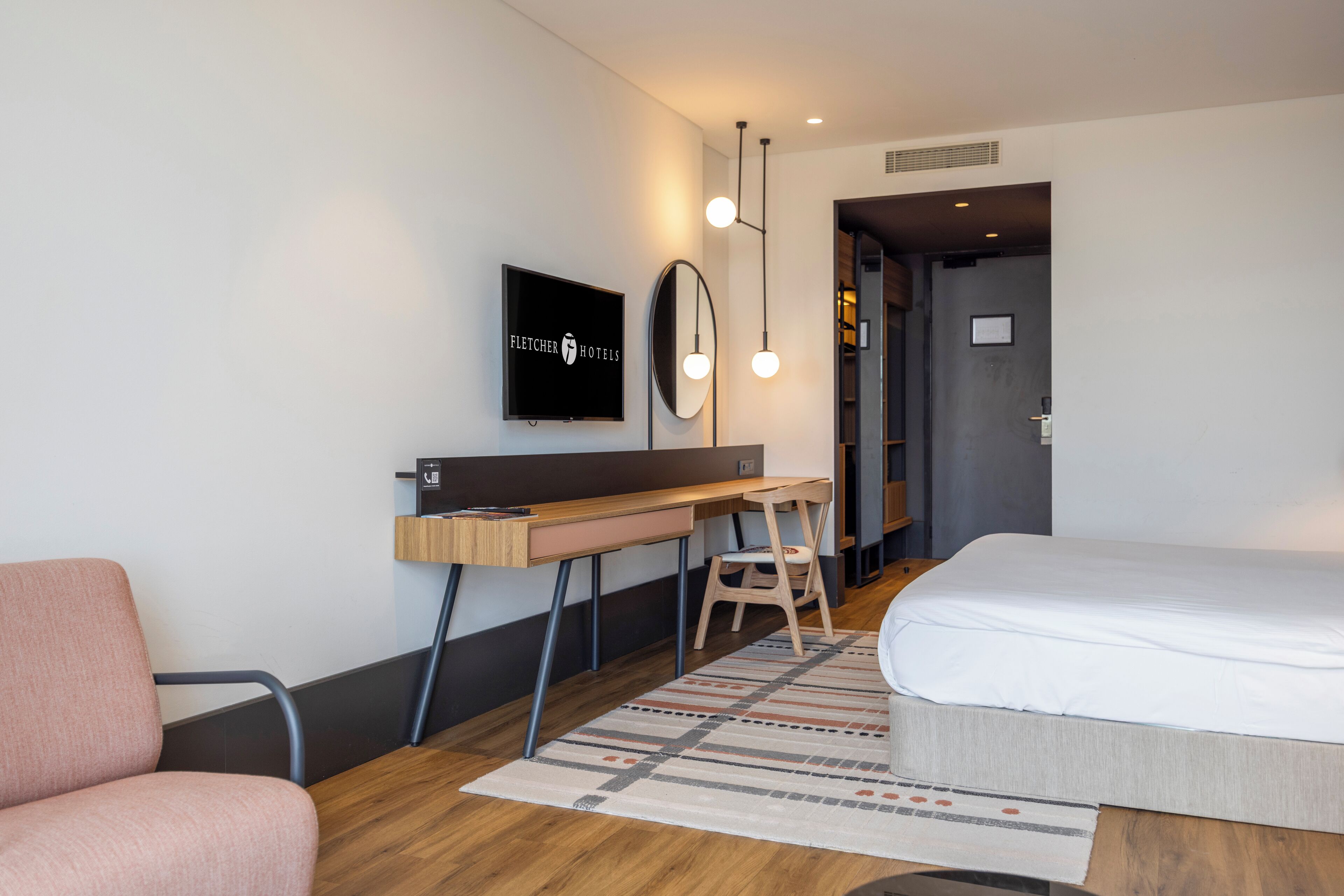 Quarto de hotel com uma cama, uma escrivaninha com cadeira, televisão e espelho.