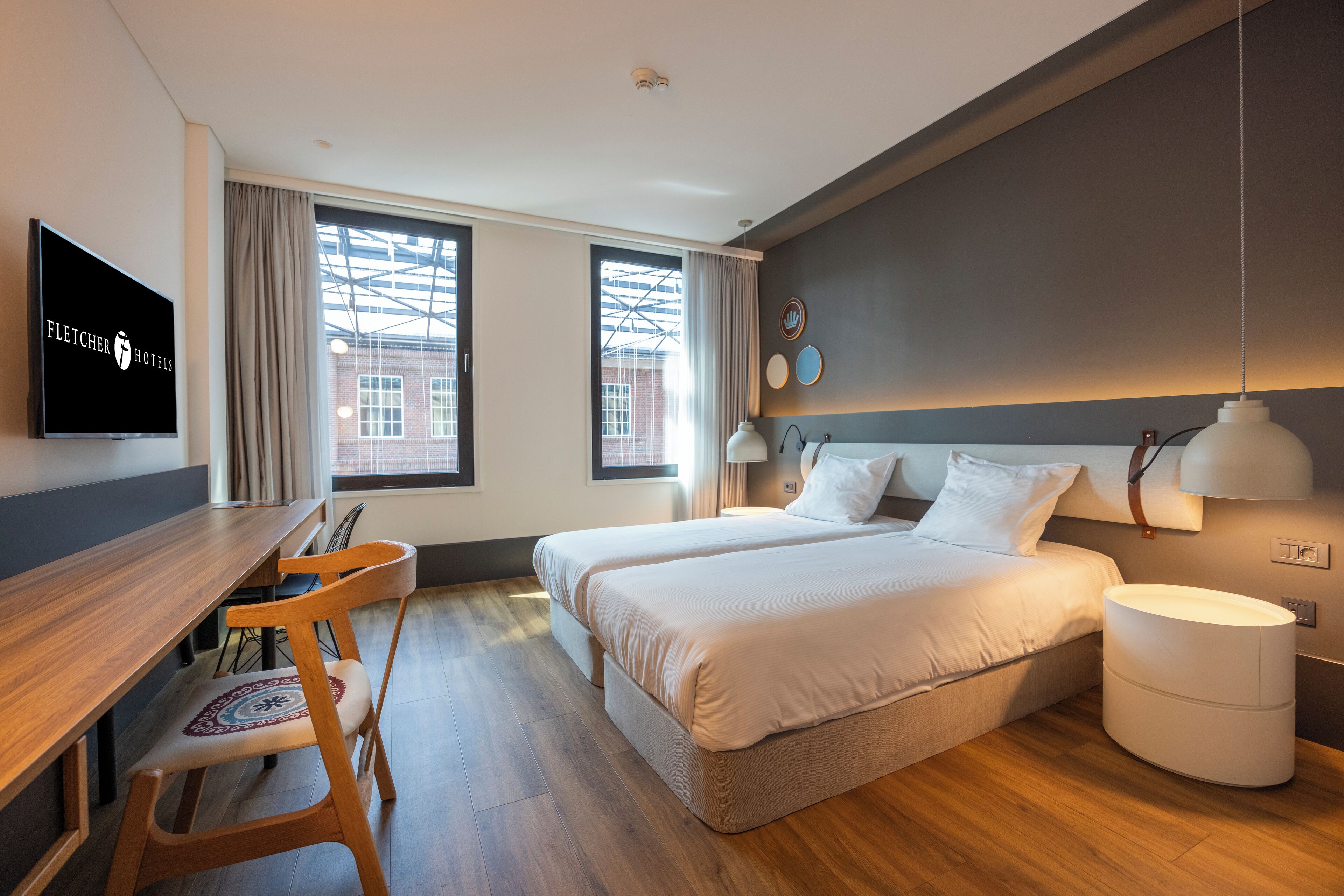 Une chambre d’hôtel équipée d’un bureau, de deux lits, d’une chaise et d’un téléviseur affichant le nom de l’hôtel.
