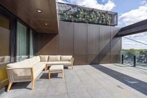 A modern outdoor seating area with a sofa and ottoman, a metal railing, and a view of the cityscape.