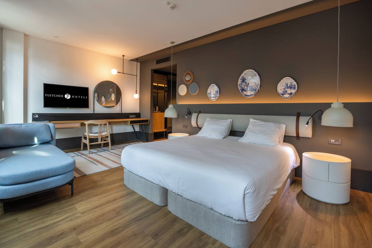 A modern hotel room with a large bed, a desk, and a television.
