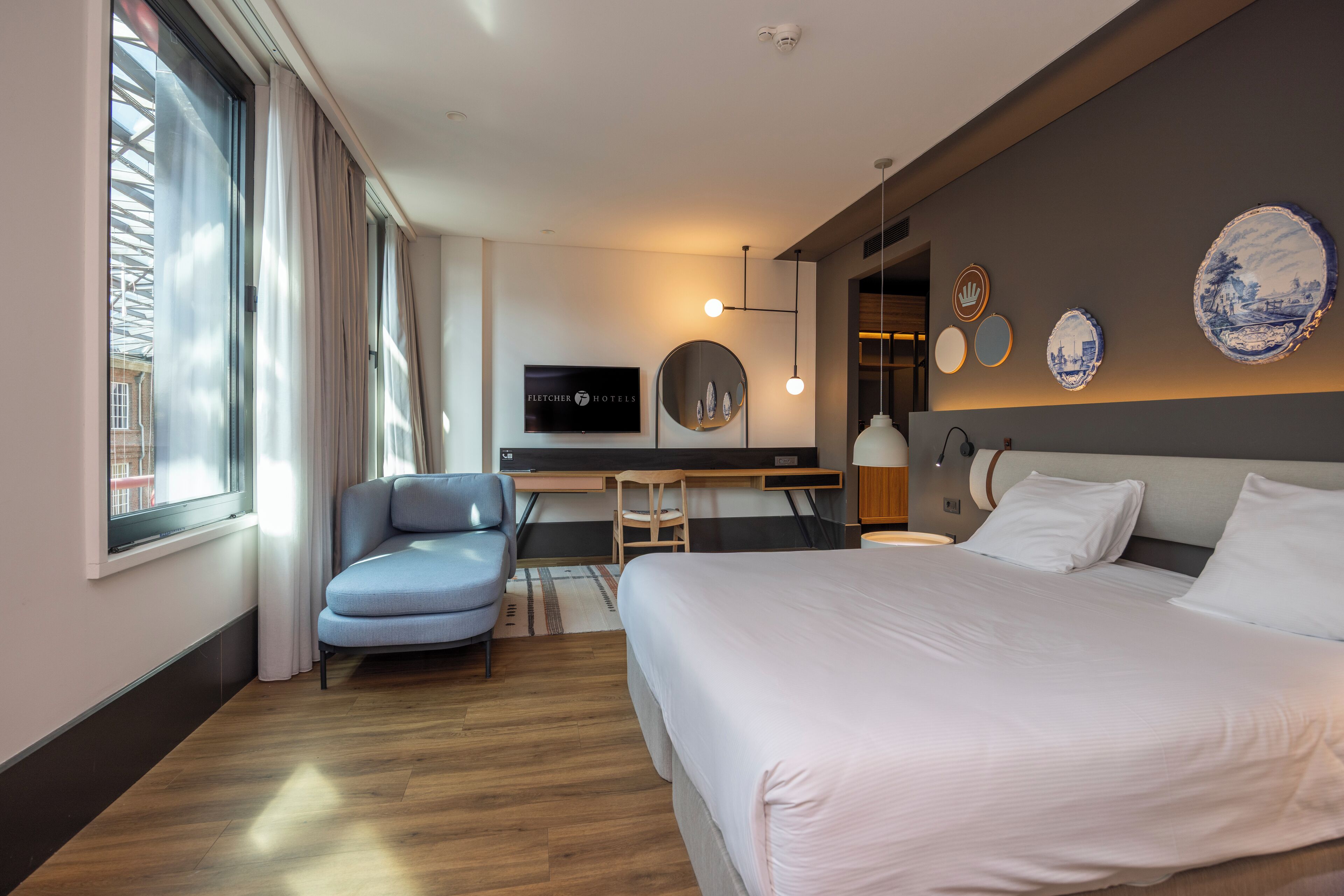 Ein modernes Hotelzimmer mit einem großen Bett, einem Schreibtisch, einem Sessel und einem Fernseher an der Wand.
