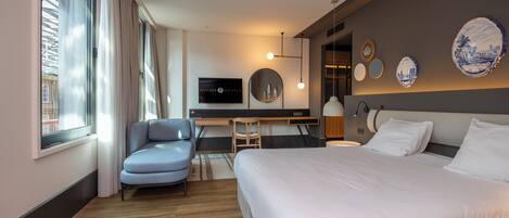 Una habitación de hotel moderna con una cama grande, un escritorio, una silla y un televisor en la pared.