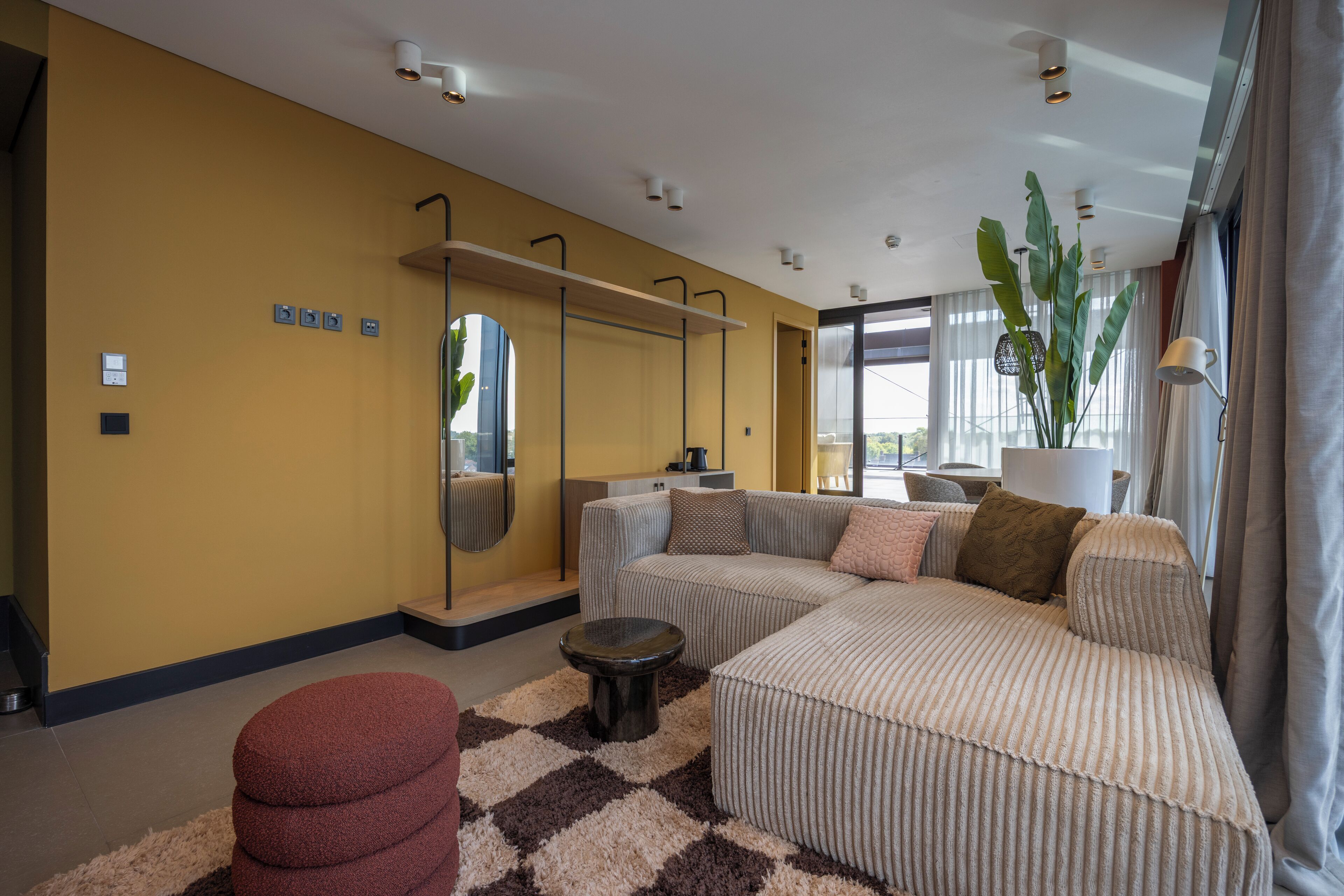Una sala de estar moderna con un amplio sofá modular, un otoman redondo y un espejo en la pared.