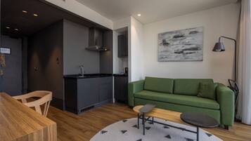 A modern living room with a green sofa, a wooden dining table, and a kitchen area in the background.