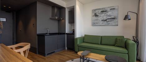 A modern living room with a green sofa, a wooden dining table, and a kitchen area in the background.
