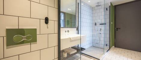 Un baño moderno con cabina de ducha de vidrio, un lavamanos con espejo y un dispensador de papel higiénico en la pared.