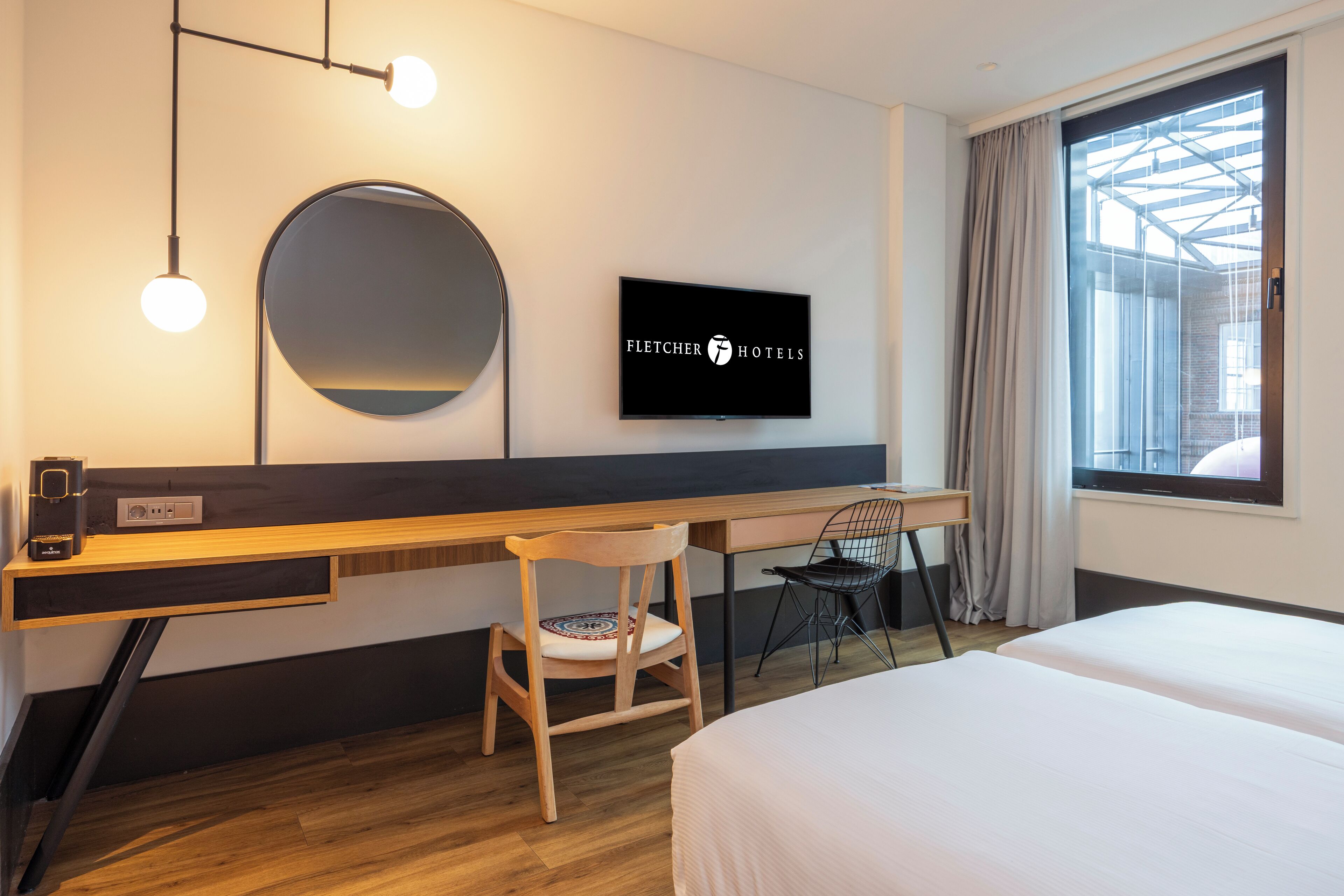 Une chambre d’hôtel comprenant un lit, un bureau avec une chaise, une télévision et une grande fenêtre avec des rideaux.