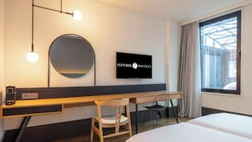 Une chambre d’hôtel comprenant un lit, un bureau avec une chaise, une télévision et une grande fenêtre avec des rideaux.