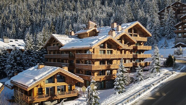 Eine mehrstöckige Holzlodge mit Balkonen, umgeben von schneebedeckten Bäumen und einem klaren Himmel.